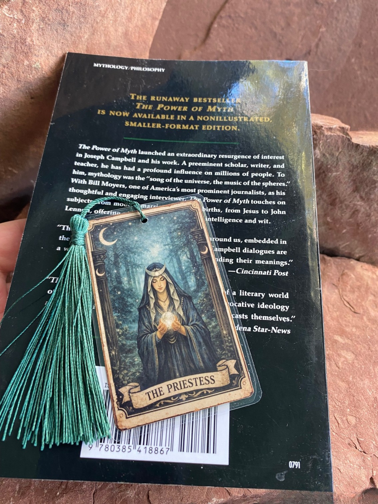 Book with tarot card and tassel on a wooden surface. Small bookmark shown ovesized paperback for scale reference only