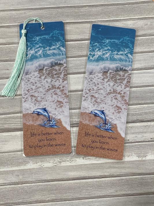 Two beach-themed bookmarks with dolphins on a wooden surface