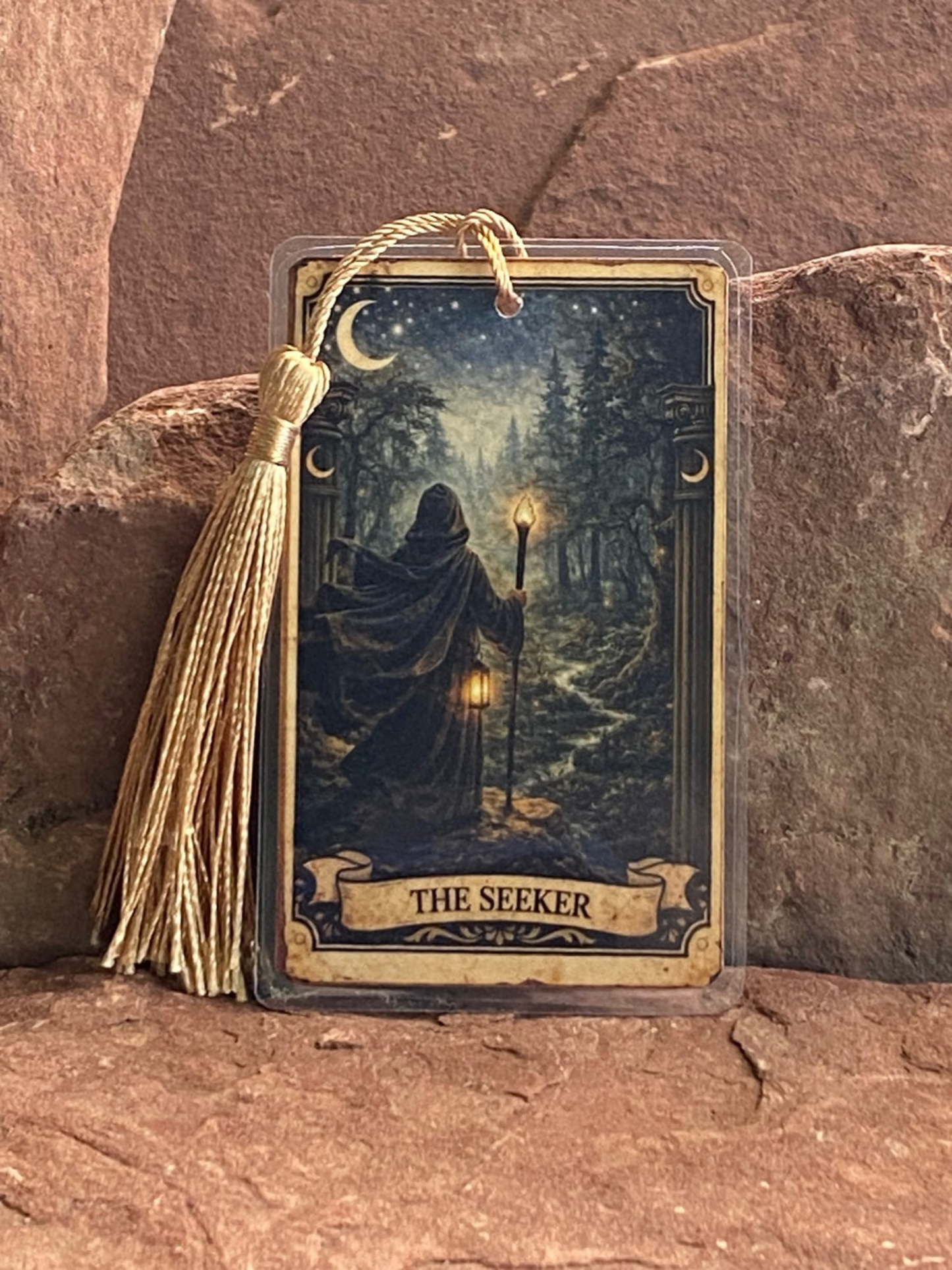 Card with 'The Seeker' design featuring a figure in a cloak holding a lantern, on a stone surface.