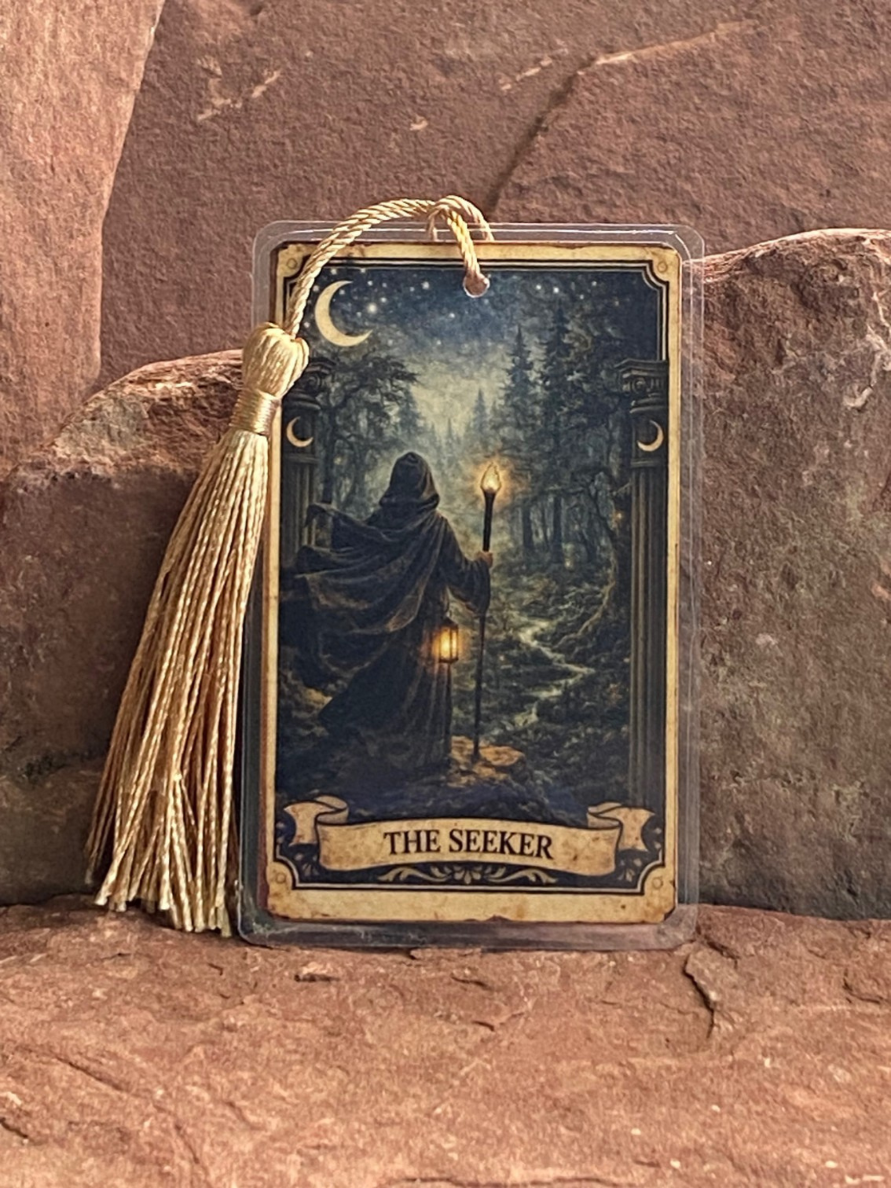Card with 'The Seeker' design featuring a figure in a cloak holding a lantern, on a stone surface.