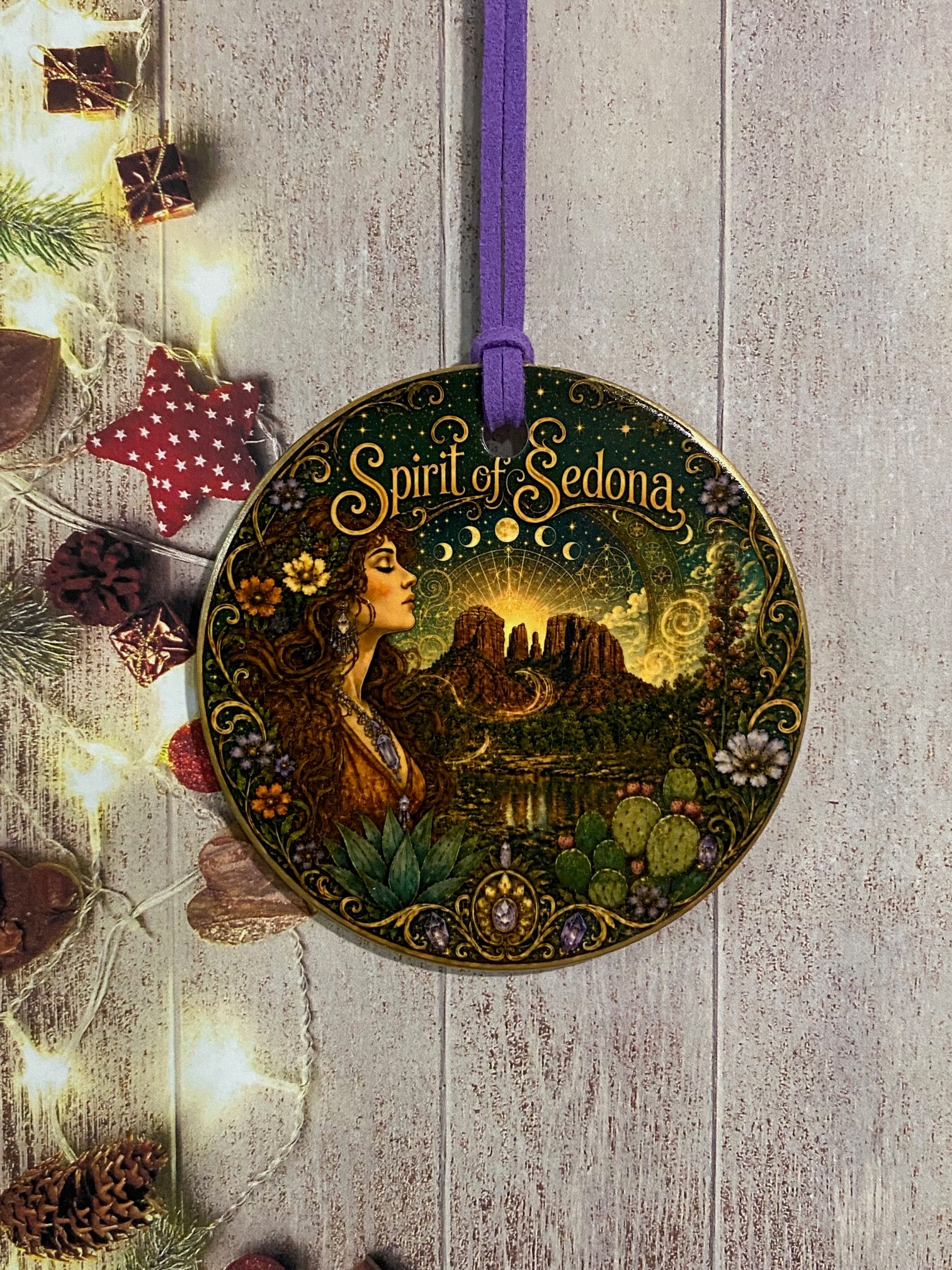 A round decorative ornament featuring an illustrated fairy in a forest with the text 'Spirit of Sedona' on a purple ribbon, displayed on a rustic wood background with fairy lights and holiday decorations.