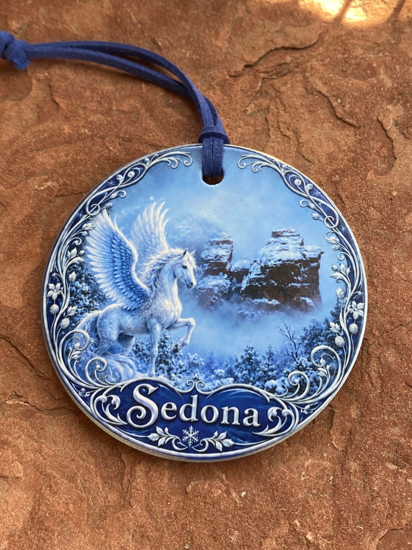 A round blue and white ceramic ornament featuring a polar bear illustration and the name 'Sedonas' on a textured brown rock surface.