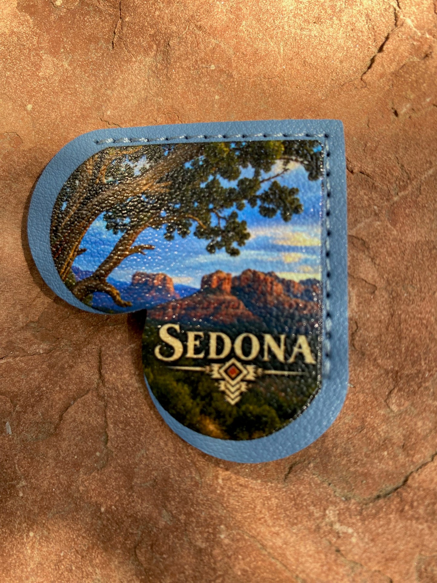 A heart-shaped leather patch with a blue border and a printed scenic design of Sedona, Arizona, featuring a tree, mountains, and the text 'SEDONA' on a textured brown rock background.